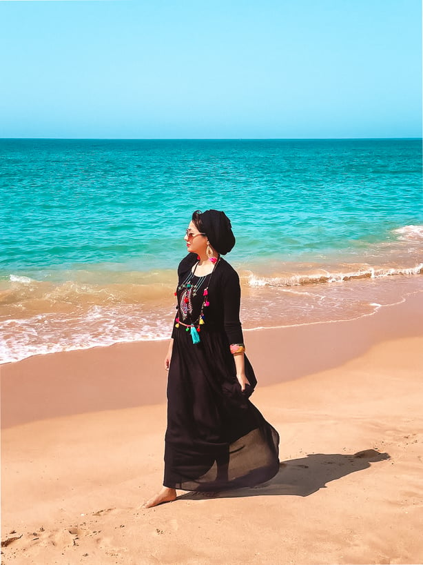 Muslim blogger walking on beach wearing black dress