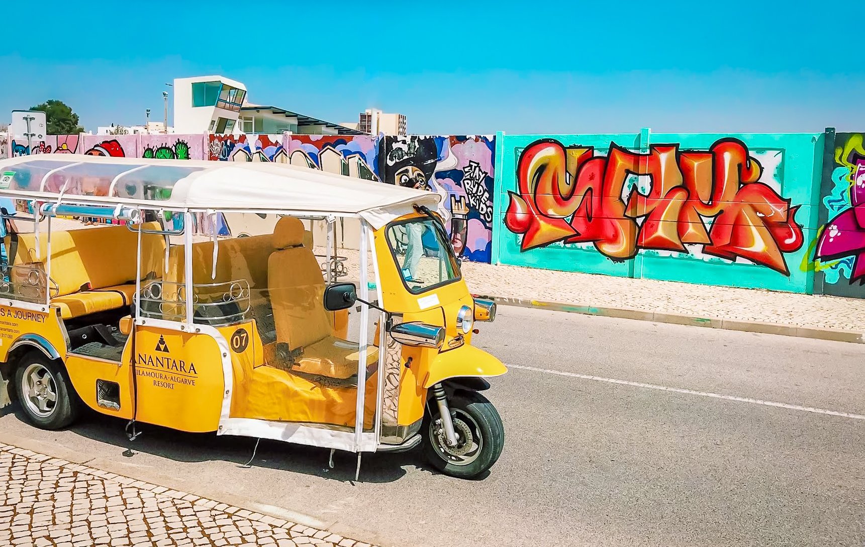 Yellow tuk-tuk beside graffiti wall 