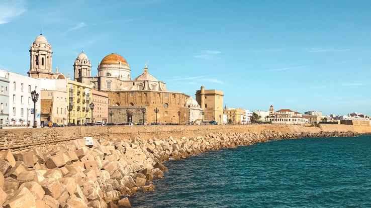 Buildings and rocks by Cadiz pier next to water