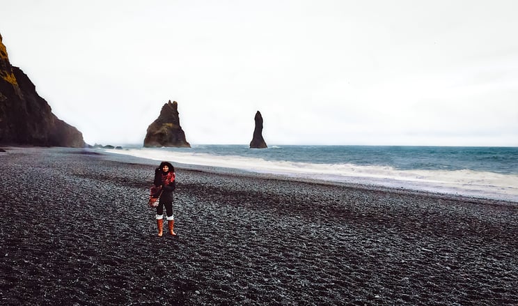 Woman alone on black sand beach with basalt sea rocks