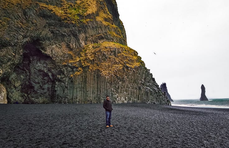 Man in front of basalt cave on black sand beach