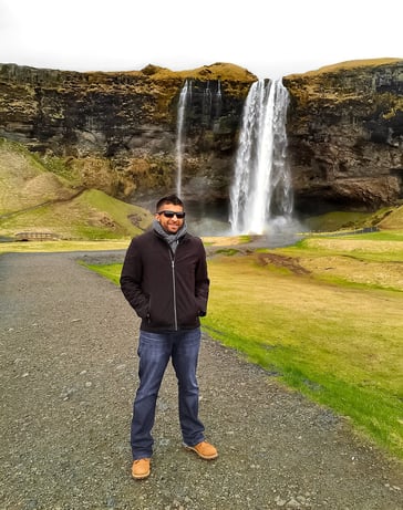 Man wearing black jacket beside waterfall