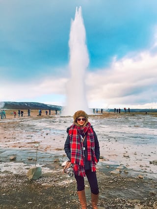 Woman wearing red scarf in front of erupting geyser