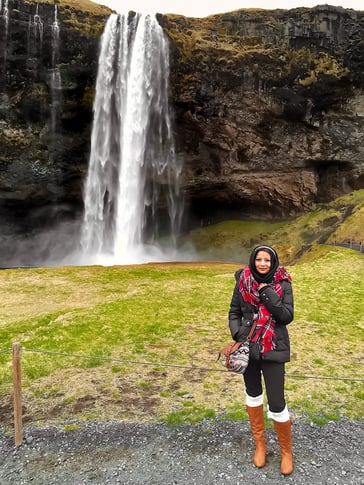 Muslim blogger wearing black jacket next to waterfall