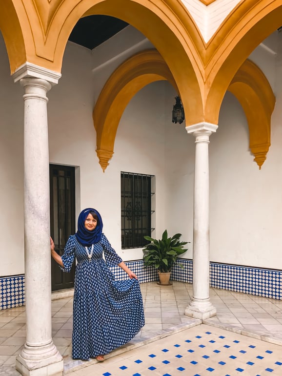 Muslim woman in blue dress in tiled courtyard underneath yellow arches Seville