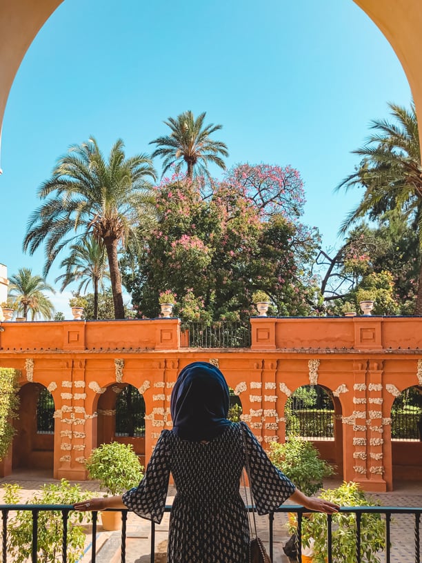 Muslim woman overlooking gardens with palm trees and arches at Seville Alcazar
